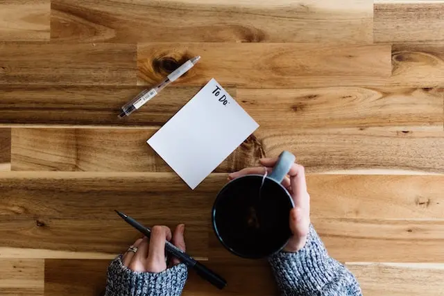 A woman making a to-do list with a cup of coffee