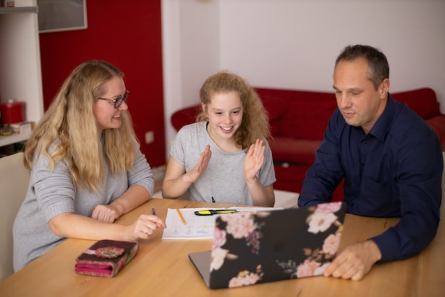 Parents and their daughter sitting at a table and looking at a laptop together