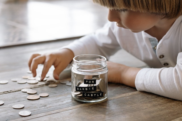 Little kid putting money into a jar and saving for a toy.