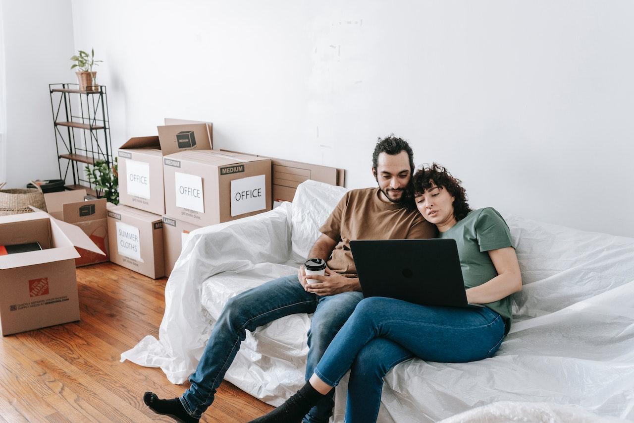 A couple sitting on the couch, surrounded by moving boxes.