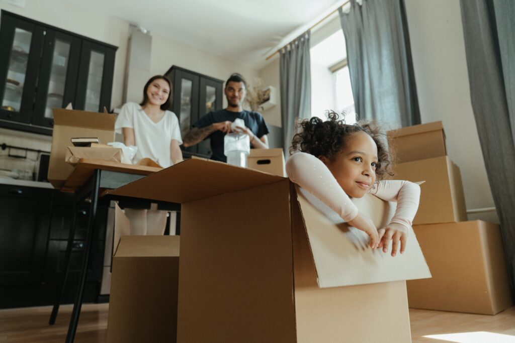 Little girl in a box with adults in the background.