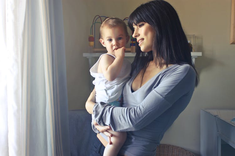 Dark-haired woman in a gray shirt holding a baby