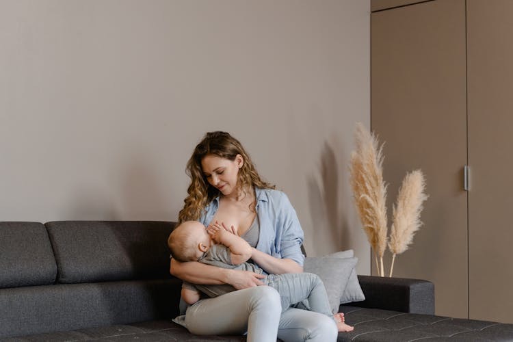 Woman in a blue shirt breast-feeding a baby on a black couch