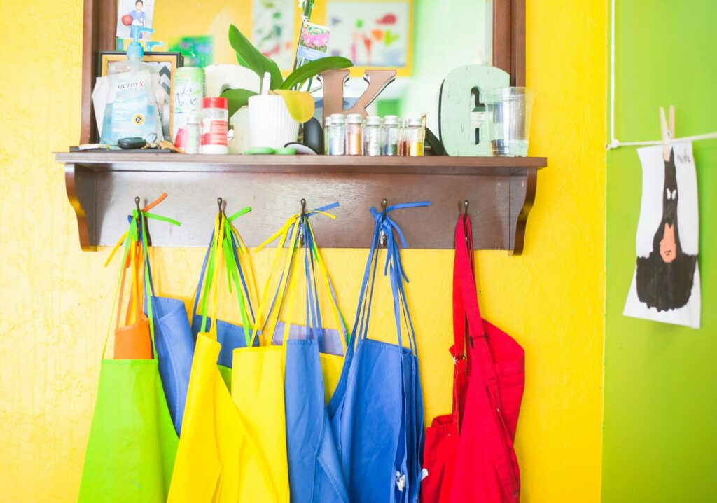 Shelve with art supplies, plant and cleaning products, with colorful fabrics on hangers, and Batman drawing on a line