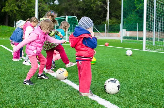 Kids in jackets and vests playing soccer. 